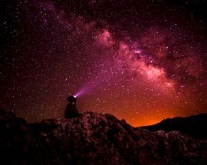 silhouette photo of person holding flashlight under milk way